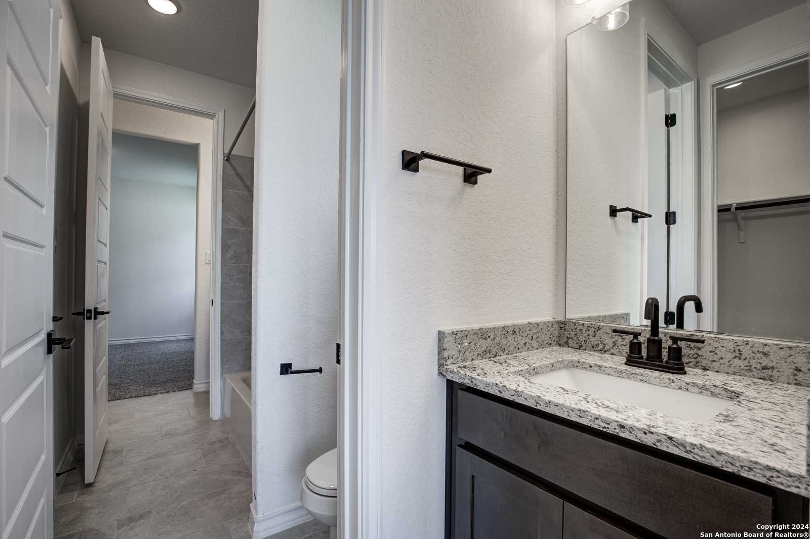 Elegant primary bathroom with quartz vanity, single sink, large mirror, and adjacent walk-in closet in Davidson Homes The Garner B, Castroville, Texas