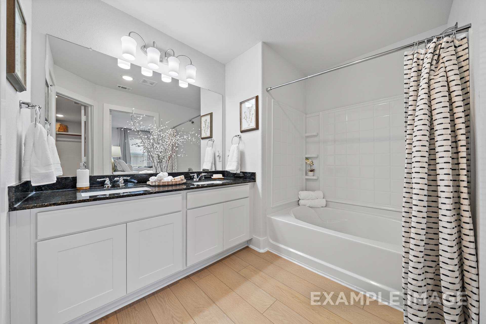 Spacious master bathroom in The Rose B with double black granite vanity, soaking tub, and patterned shower curtain