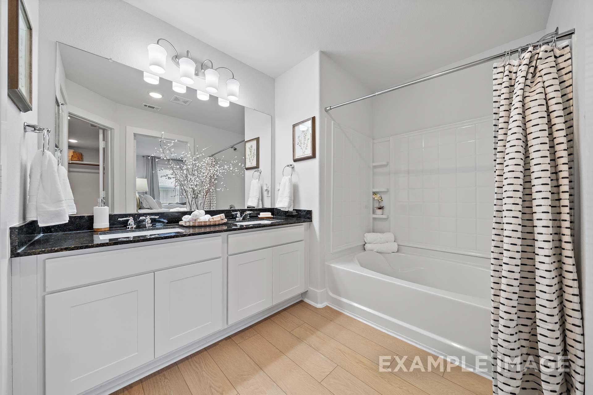 Spacious master bathroom in The Rose B with double black granite vanity, soaking tub, and patterned shower curtain
