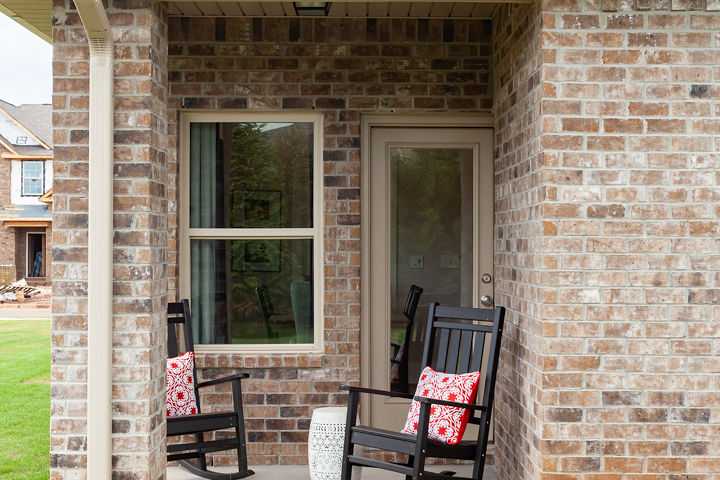 Brick home exterior with covered porch, black rocking chairs, red pillows, and side table at Williams Pointe in Huntsville, Alabama
