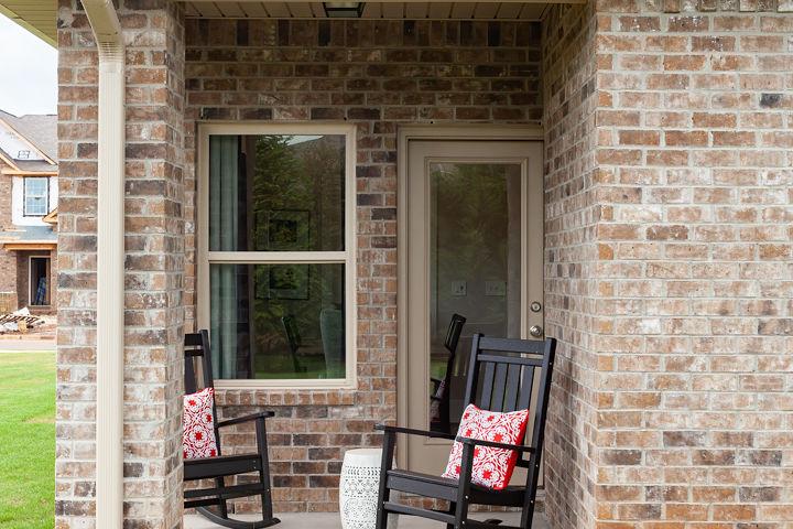 Brick home exterior with covered porch, black rocking chairs, red pillows, and side table at Williams Pointe in Huntsville, Alabama