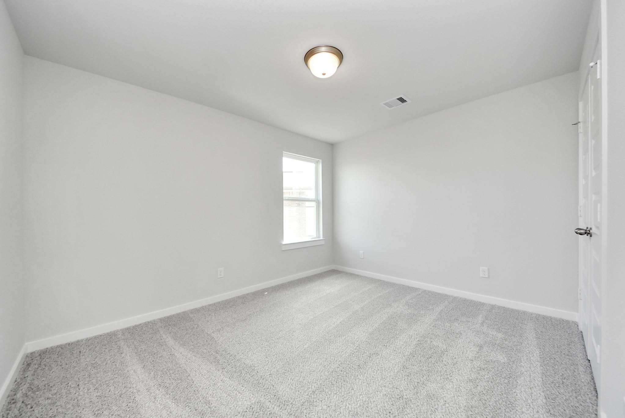 Bright, carpeted bedroom with neutral walls in The Verano B floor plan by Davidson Homes in Sunterra, Katy, Texas.