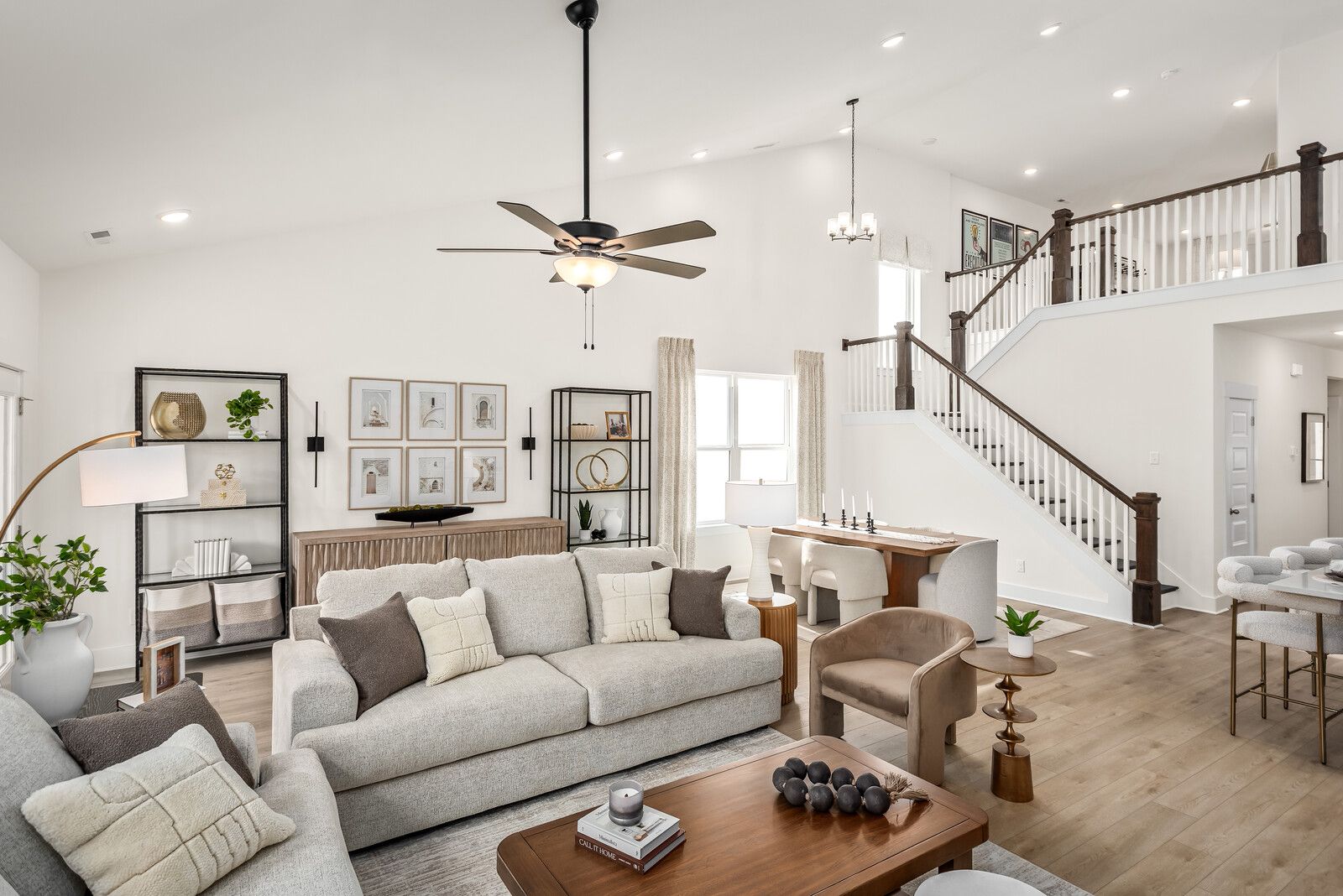 Spacious two-story living room in The Ridgeport E with vaulted ceilings, wooden staircase, beige sofa, coffee table, and open bar area