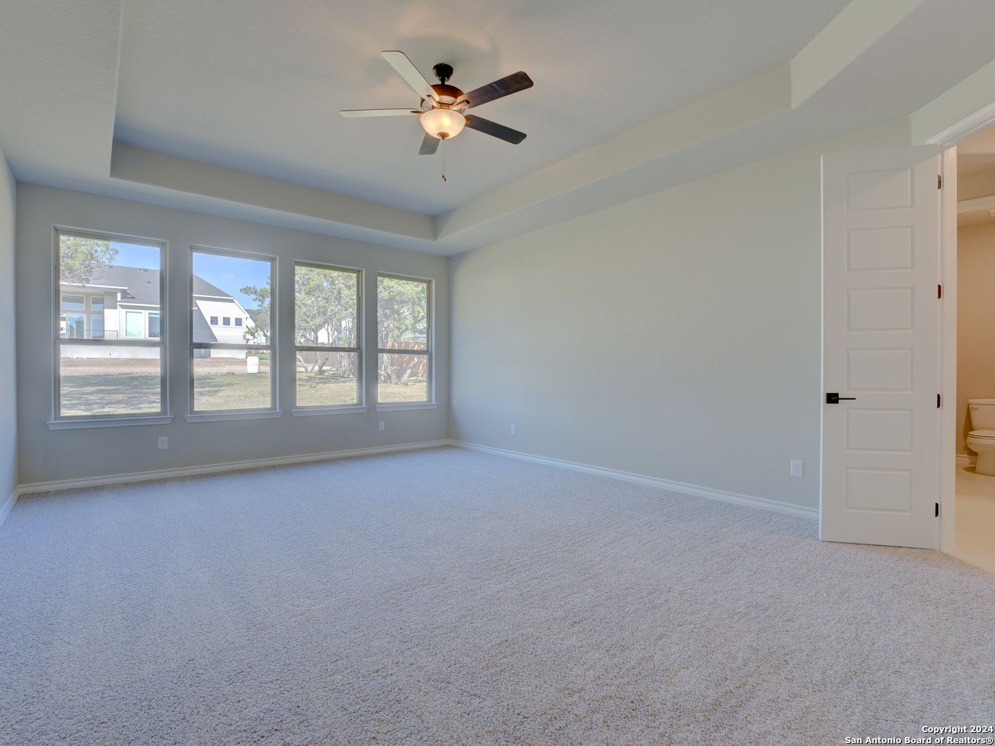 Spacious master bedroom with ceiling fan, large windows overlooking backyard, and en-suite bath in Davidson Homes The Summerlin A, Castroville, Texas