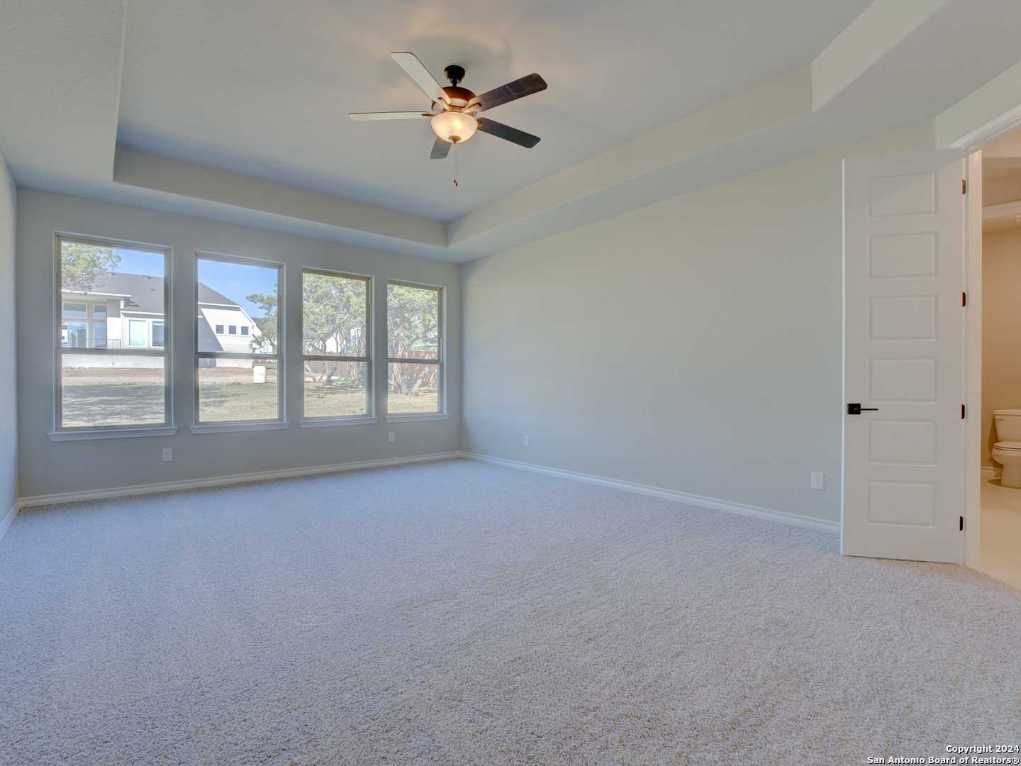 Spacious master bedroom with ceiling fan, large windows overlooking backyard, and en-suite bath in Davidson Homes The Summerlin A, Castroville, Texas