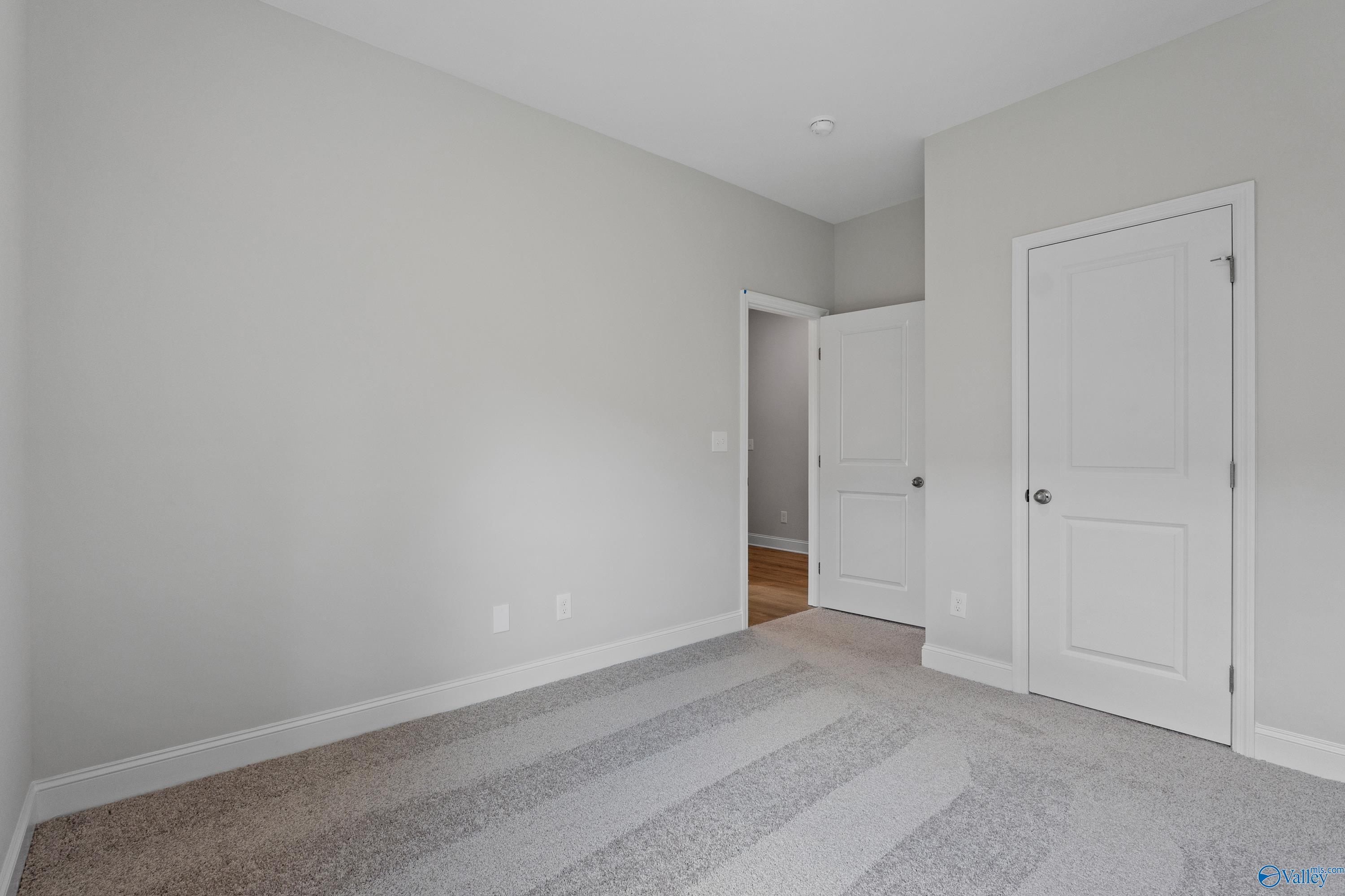 Bright secondary bedroom with light gray walls, neutral carpet, and white doors in Davidson Homes The Asheville, Huntsville AL