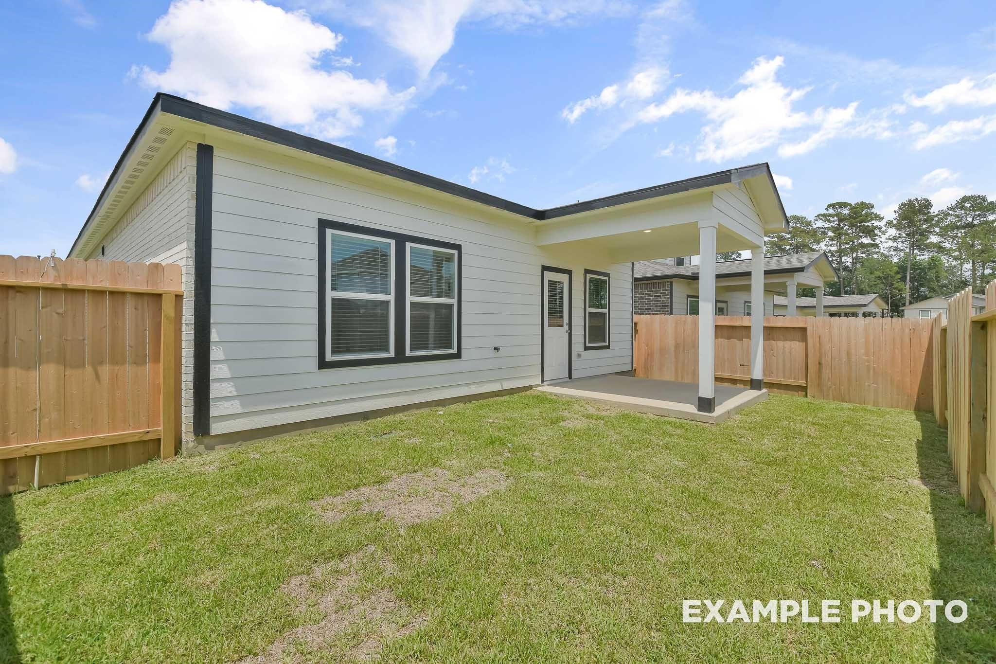 Modern single-story home exterior with black-trimmed windows, covered patio, wooden fence, and lush green yard in Conroe, Texas
