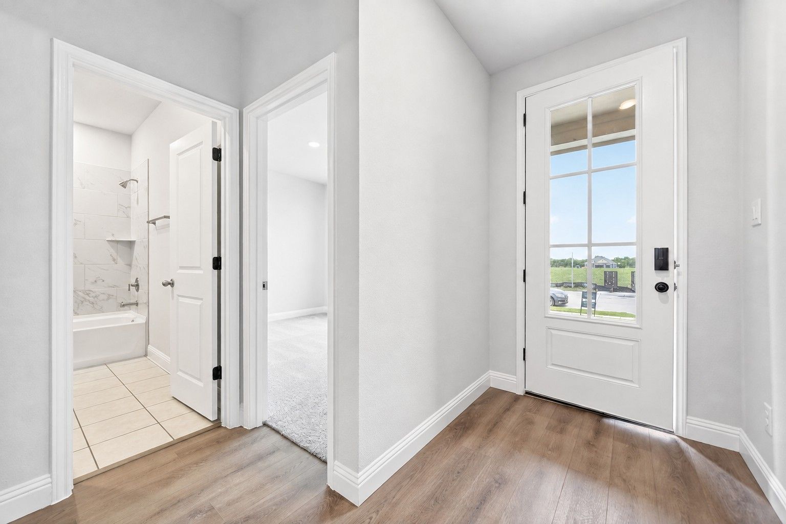 Entryway view of The Redbud C in Josephine, TX, showing wood-style flooring, a glass-paneled front door, and hallway bath.