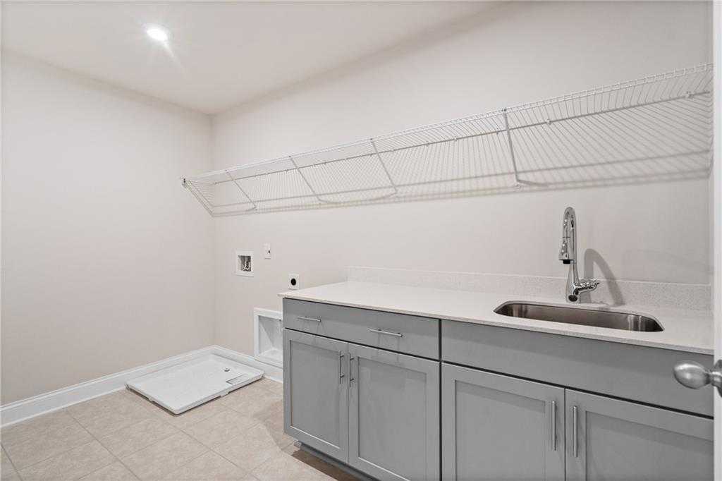 Modern laundry room featuring gray cabinets, stainless sink, wire shelving in Davidson Homes The Hickory B at Wehunt Meadows, Hoschton, Georgia