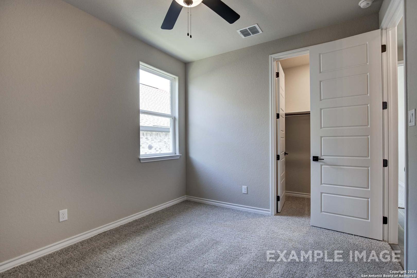 Bright bedroom featuring gray walls, carpet flooring, ceiling fan, window, and open walk-in closet in Davidson Homes The Rockford G, San Antonio