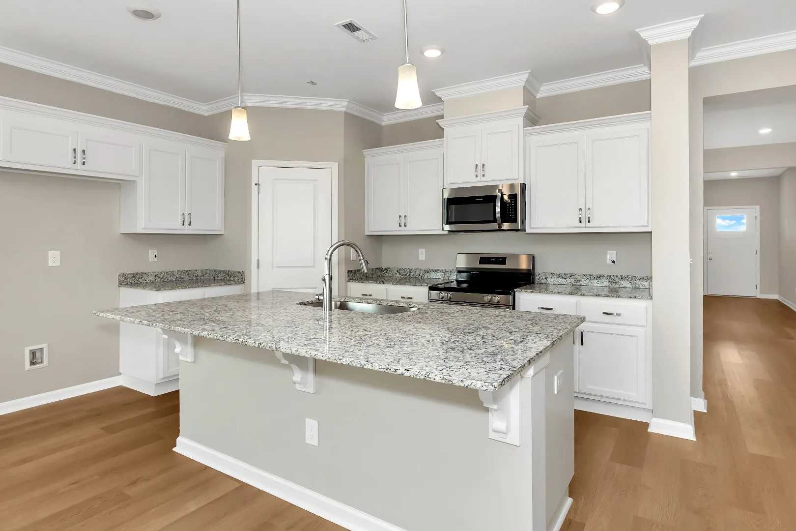 Spacious kitchen at Links Crossing in Auburn AL with white shaker cabinets, granite island, stainless appliances, and hardwood floors