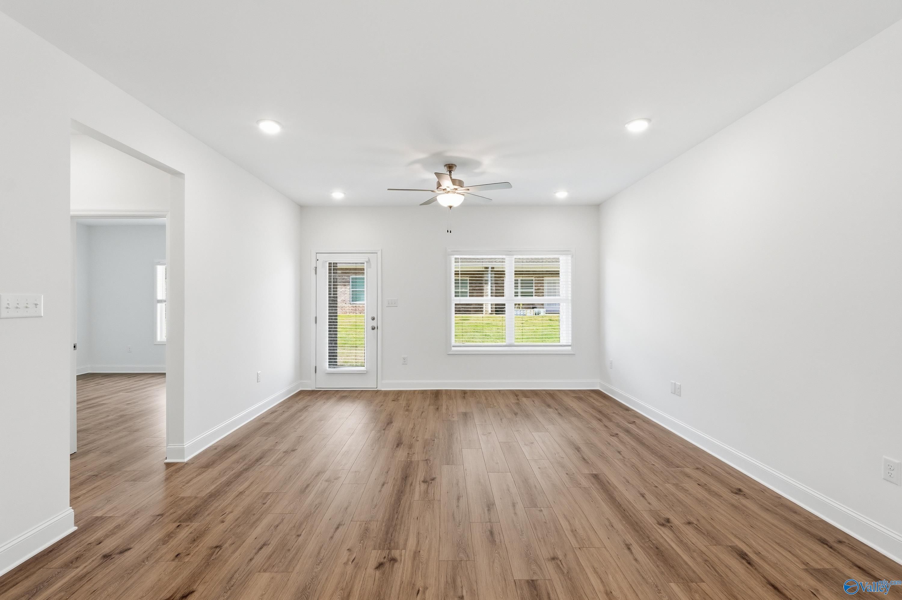 Spacious empty living room with hardwood floors, white walls, ceiling fan, and large windows overlooking yard in Davidson Homes Cumberland D, Decatur AL