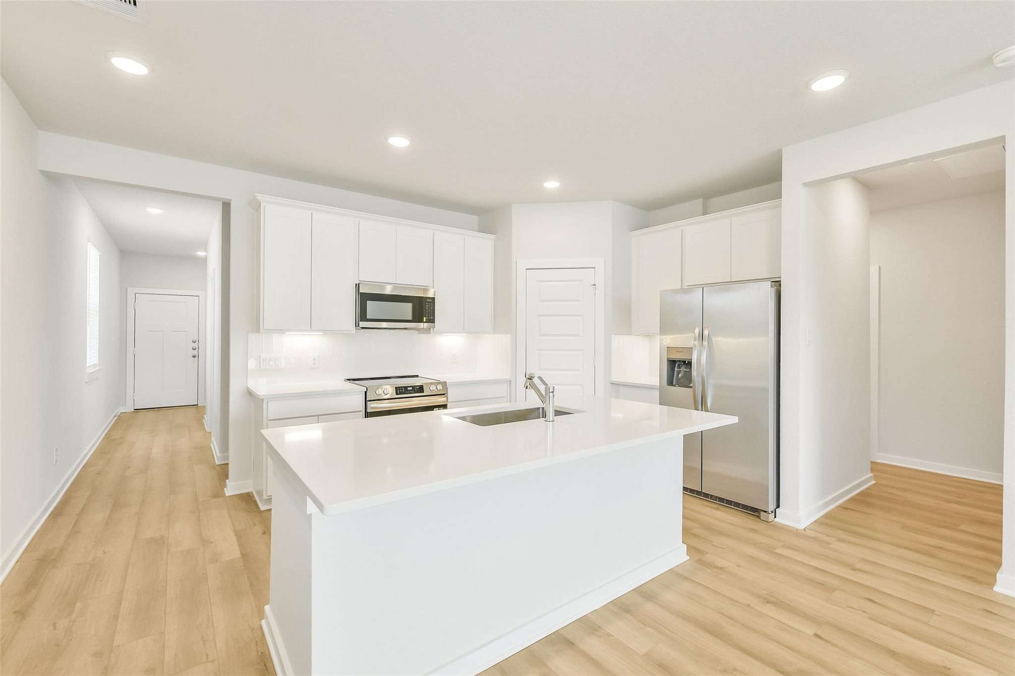 Modern open-concept kitchen with white cabinets, quartz island, stainless appliances in Davidson Homes San Marcos E, Cleveland TX