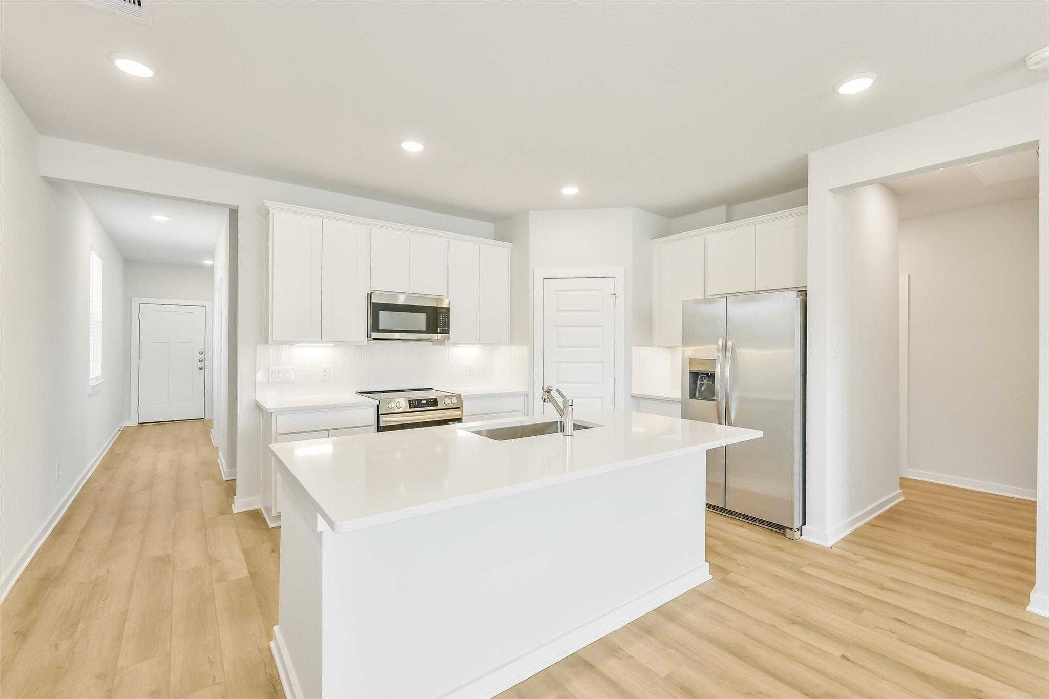 Modern open-concept kitchen with white cabinets, quartz island, stainless appliances in Davidson Homes San Marcos E, Cleveland TX