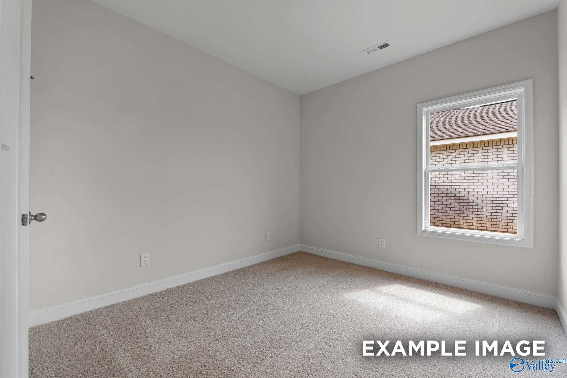 Bright empty bedroom with light gray walls, beige carpet, and window view in Davidson Homes The Butler, Toney, AL