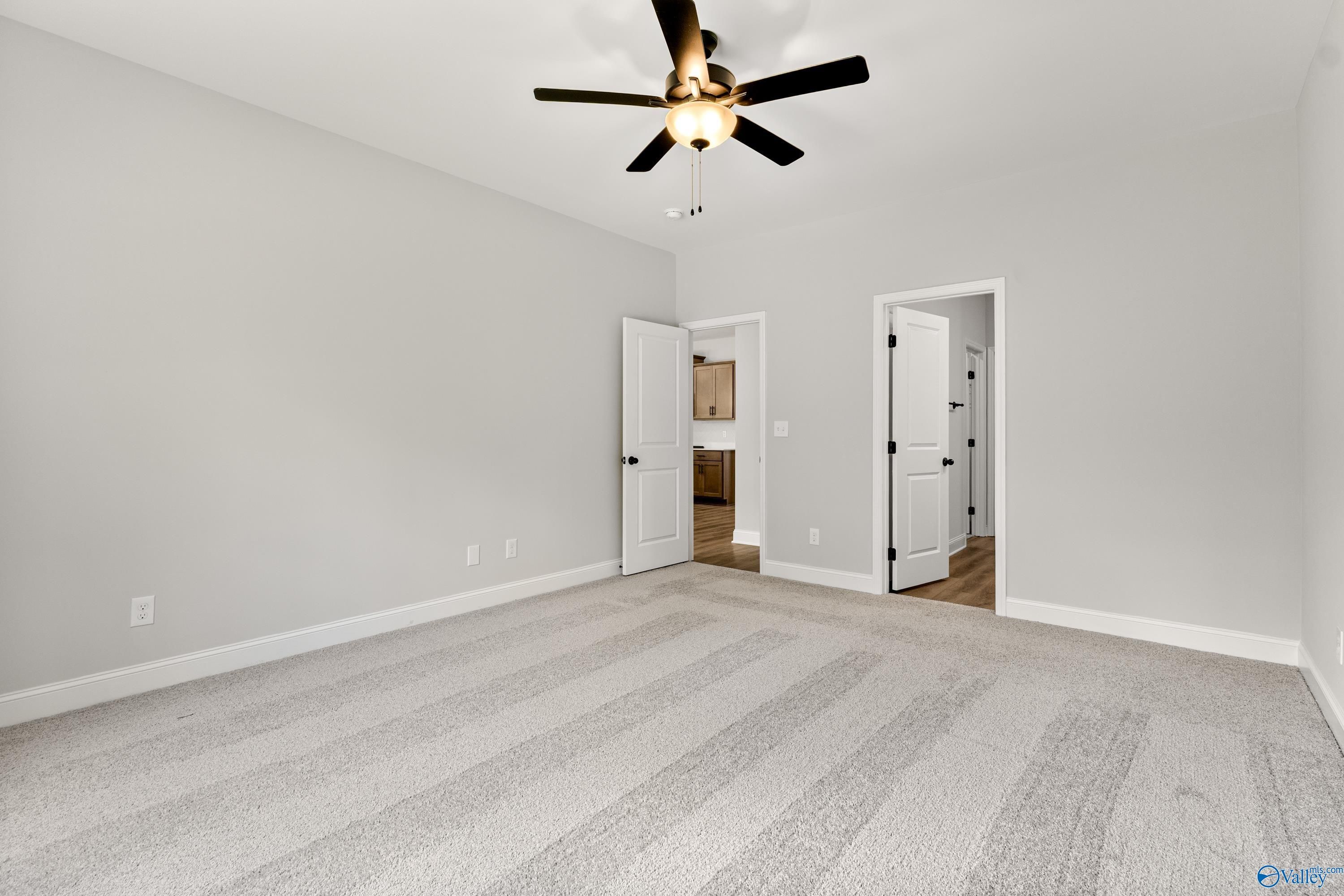 Spacious bedroom with gray carpet, ceiling fan, and doors to bathroom in Davidson Homes The Daphne, Huntsville AL