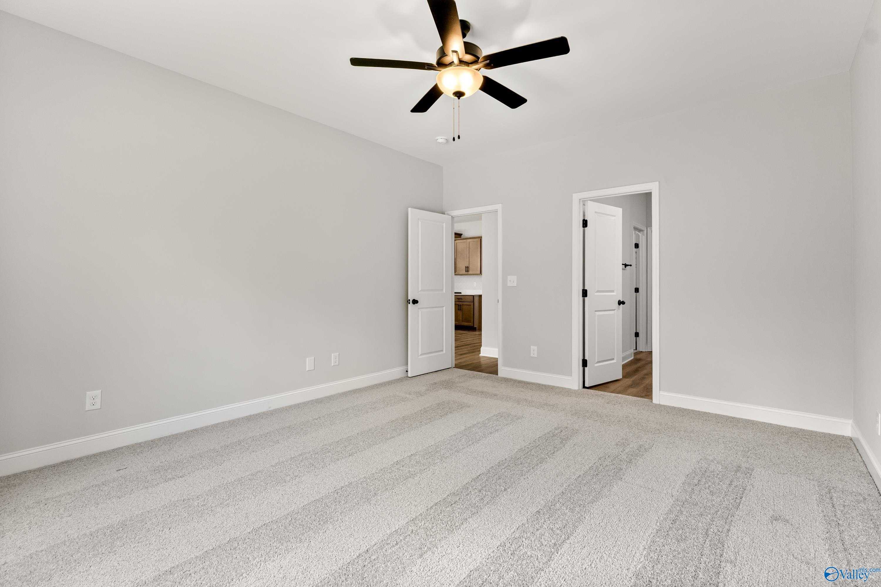 Spacious bedroom with gray carpet, ceiling fan, and doors to bathroom in Davidson Homes The Daphne, Huntsville AL