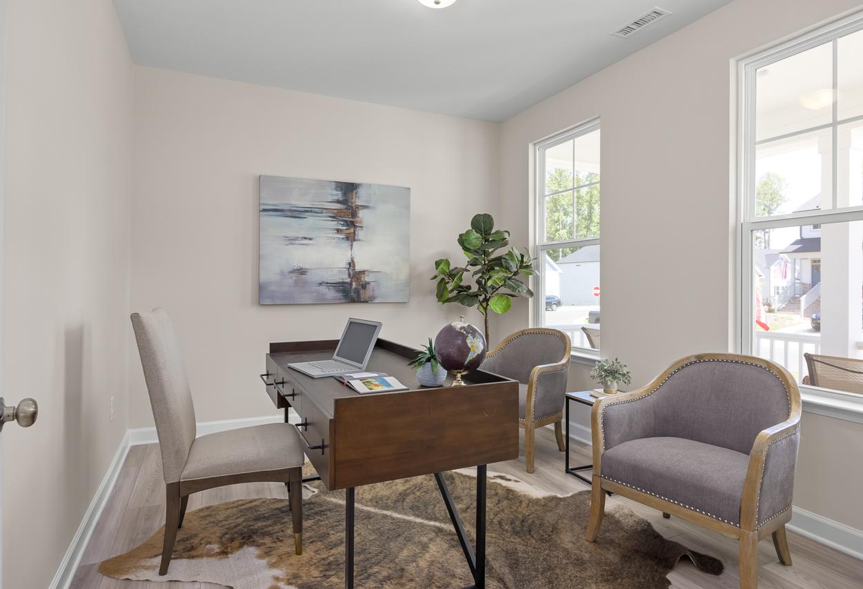 Modern home office in The Chestnut floor plan featuring a dark wood desk, two upholstered chairs, and neutral decor.