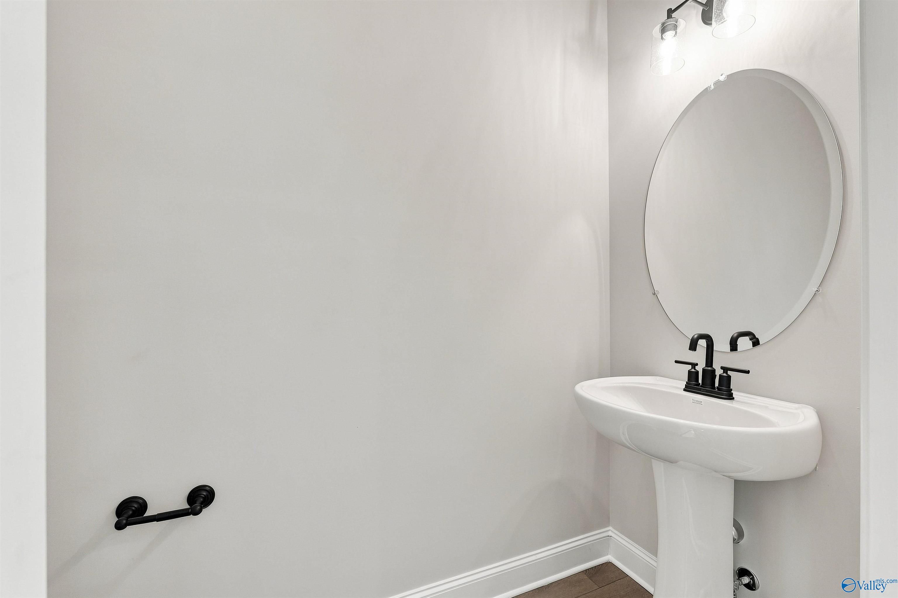 Modern half bath with pedestal sink, matte black fixtures, and round mirror in The Oxford floor plan, Kendall Farms, Toney.