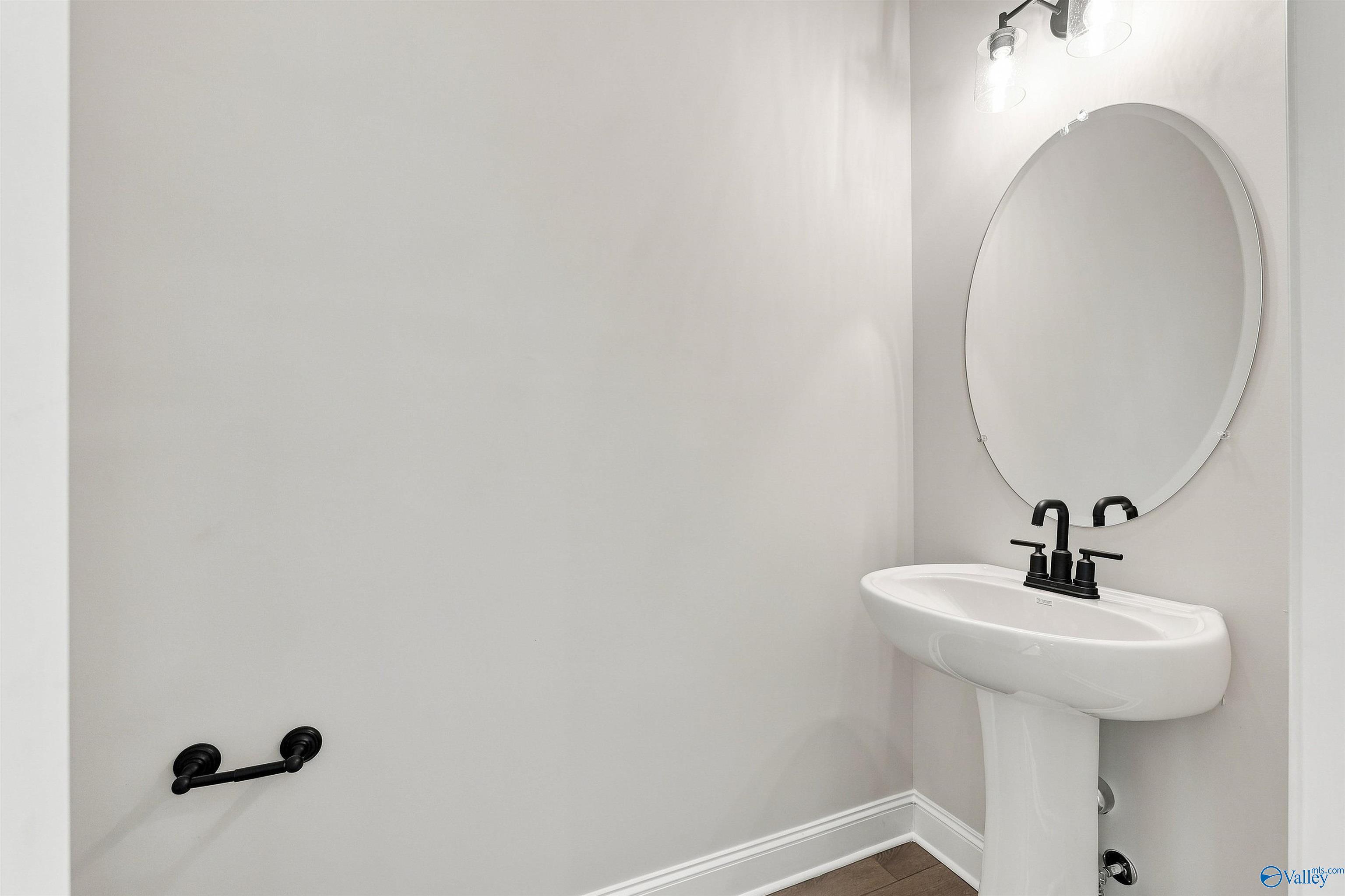 Modern half bath with pedestal sink, matte black fixtures, and round mirror in The Oxford floor plan, Kendall Farms, Toney.