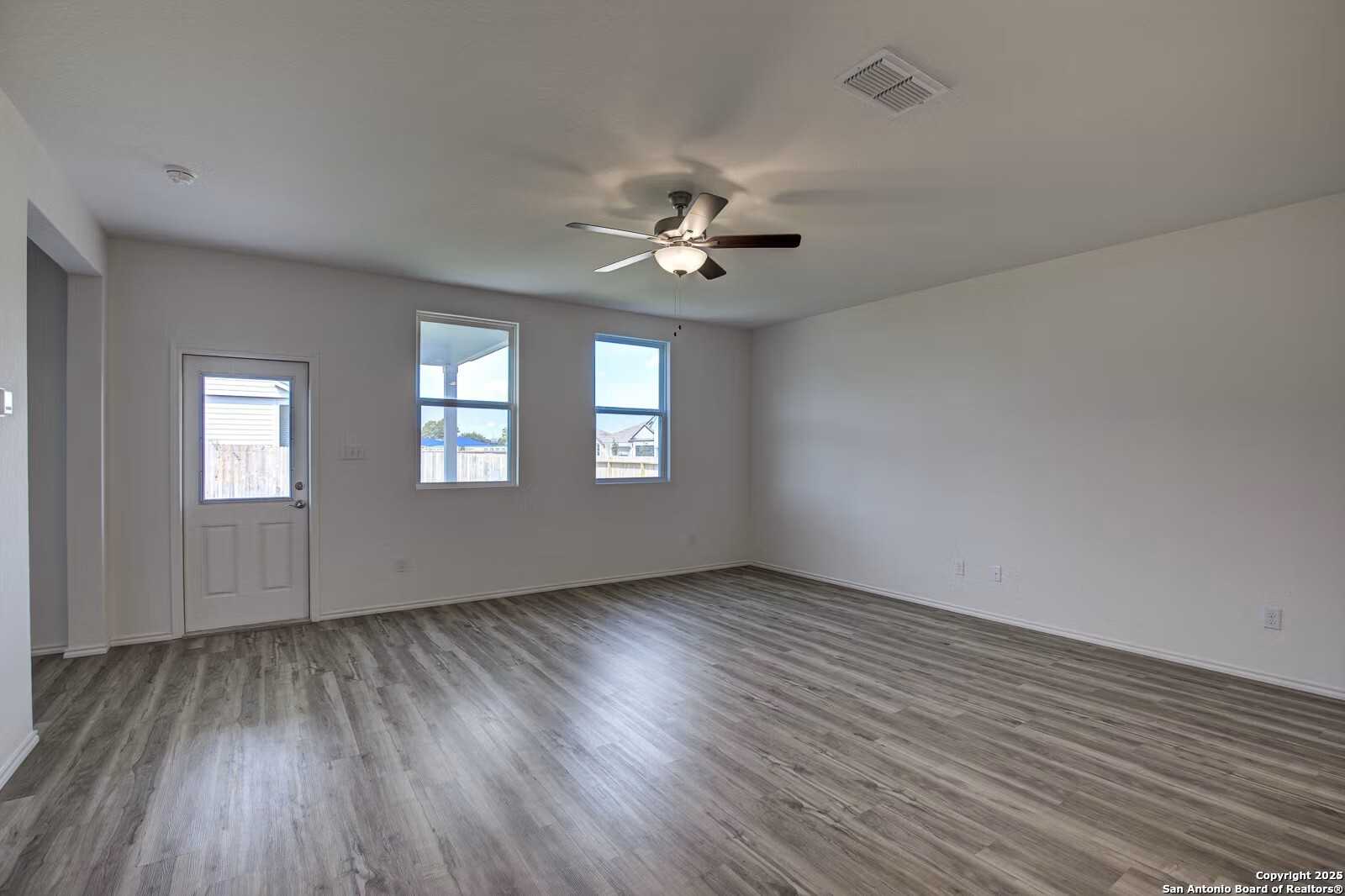 Bright living room with ceiling fan, large windows, and luxury vinyl plank flooring in Davidson Homes The Douglas B, Seguin, Texas
