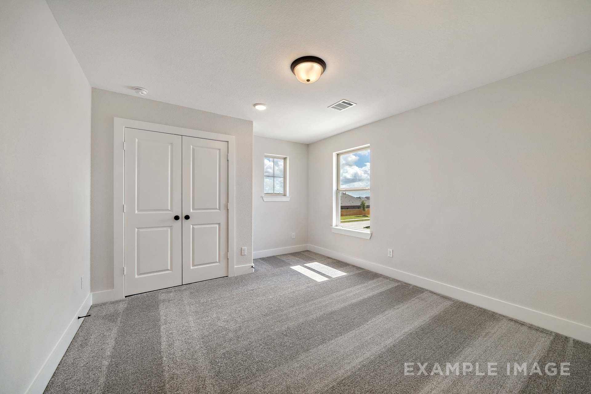 Spacious bedroom in The Victoria by Davidson Homes with white double closet doors, gray carpet, and natural light