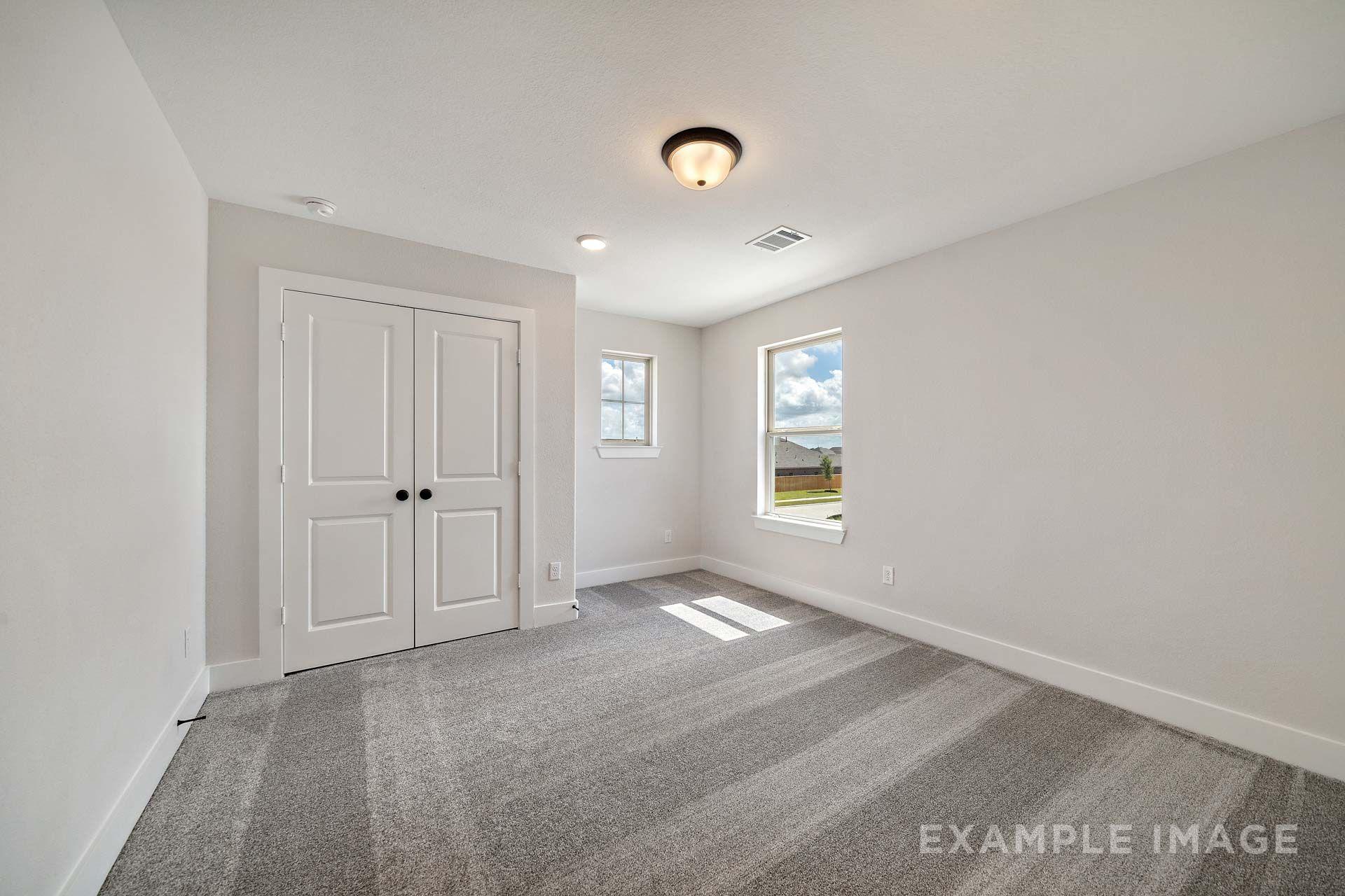 Spacious bedroom in The Victoria by Davidson Homes with white double closet doors, gray carpet, and natural light
