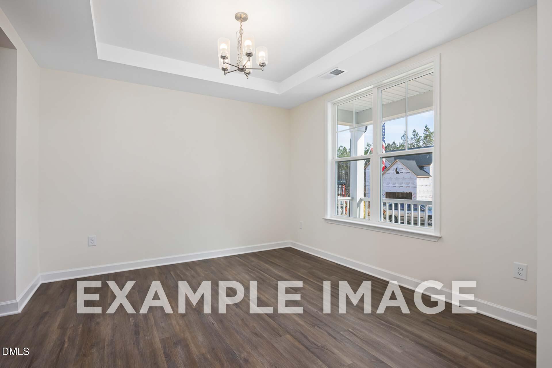 Bright empty living room with beige walls, hardwood floors, chandelier, and large window overlooking woods in The Ash B home, Zebulon NC