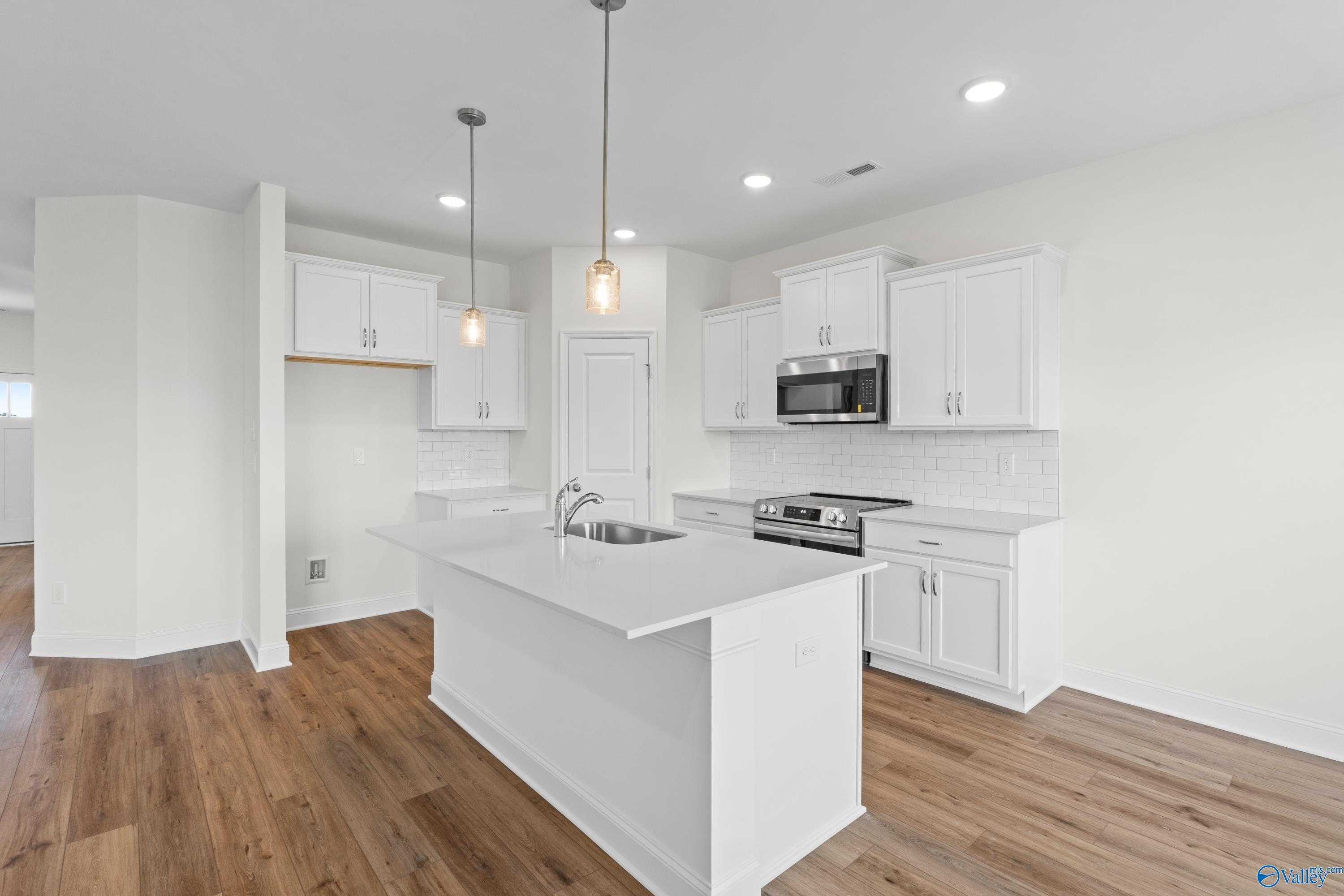 Modern white kitchen with island sink, stainless appliances, pendant lights, hardwood floors in Davidson Homes The Asheville C, Hazel Green, AL