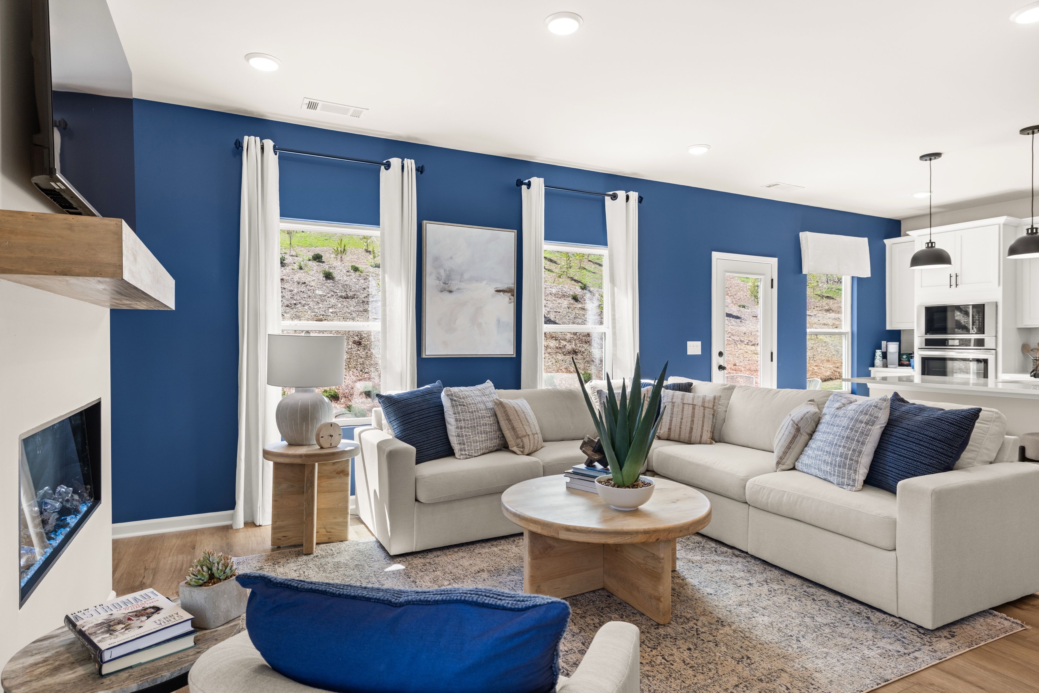 Modern open-concept living room in The Bluffs, Canton GA with navy accent wall, beige sectional sofa, and gas fireplace