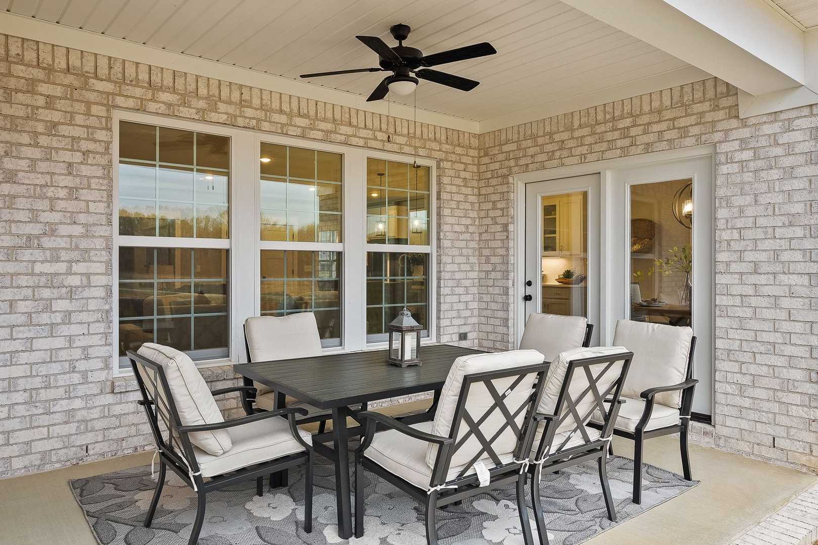 Spacious covered patio of The Oxford home with brick exterior, ceiling fan, and rectangular dining table set for six