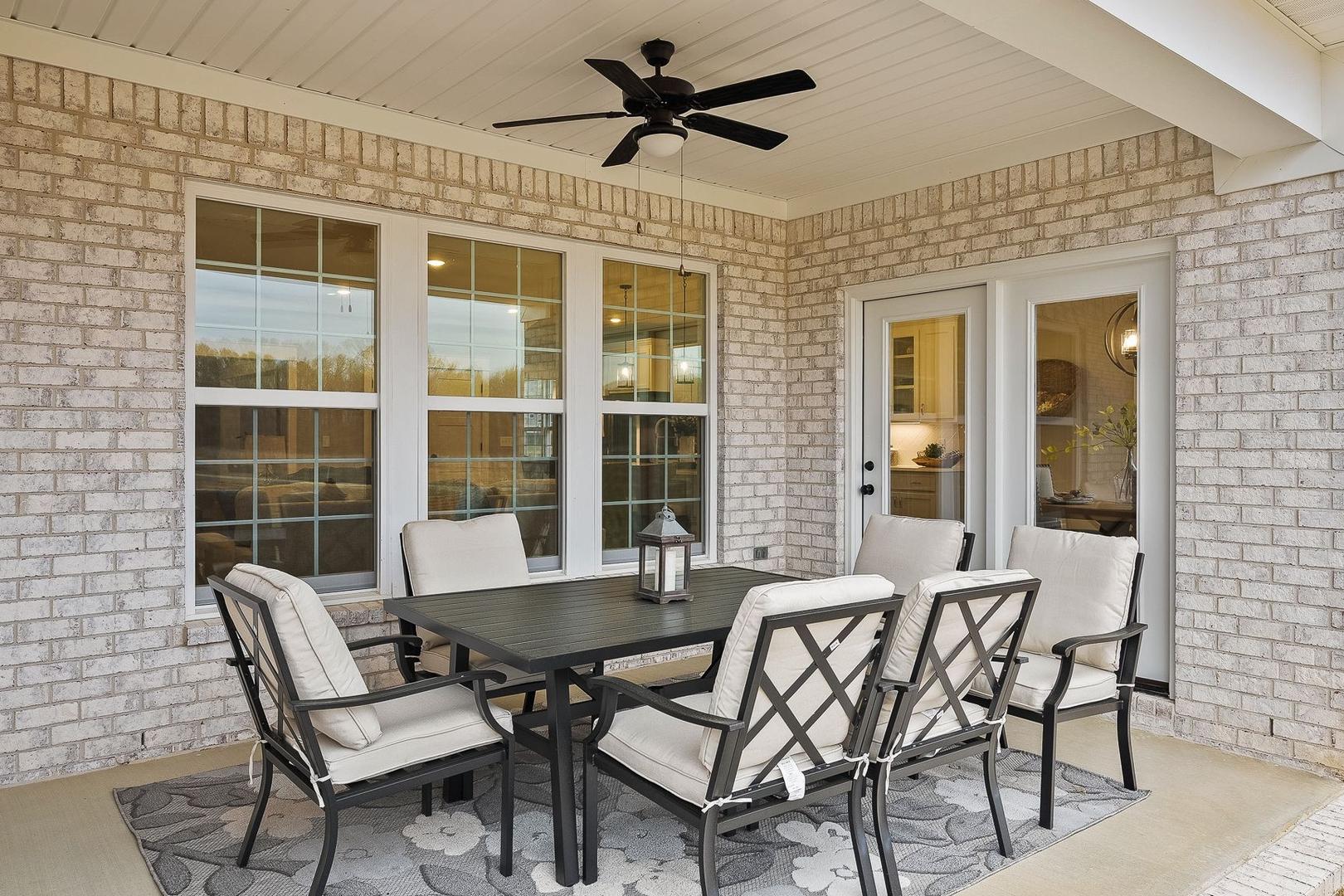Spacious covered patio of The Oxford home with brick exterior, ceiling fan, and rectangular dining table set for six