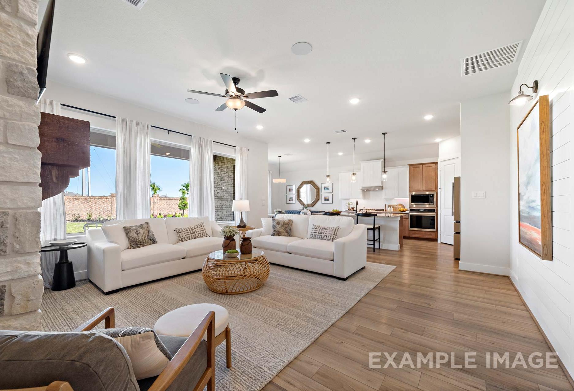 Spacious open-concept living room in The Edward A with white sofas, stone fireplace, and adjacent modern kitchen island