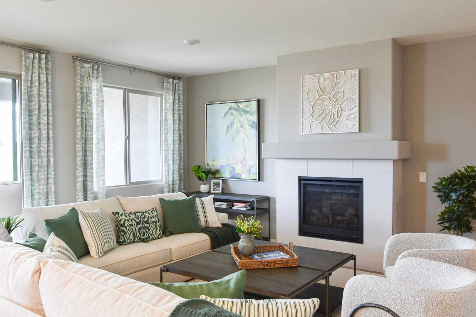 Cozy living room in The Harmony Davidson Homes with green sectional sofa, modern white fireplace, and large curtained windows