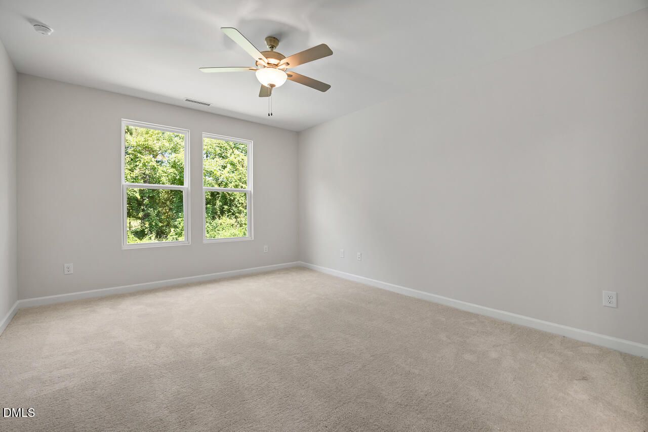 Bright bedroom with carpet, ceiling fan, and double windows overlooking trees in Davidson Homes The Daphne D, Zebulon NC