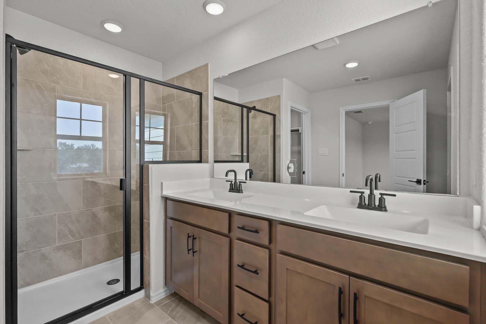 Modern master bathroom in The Florence B featuring a dual-sink vanity and tiled walk-in shower with black fixtures.