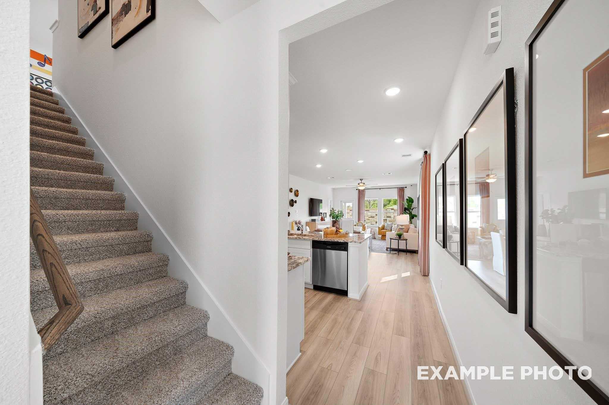 Bright hallway with carpeted staircase, light wood floors, and open kitchen island in The Sabine F 4-bedroom home, Magnolia, Texas