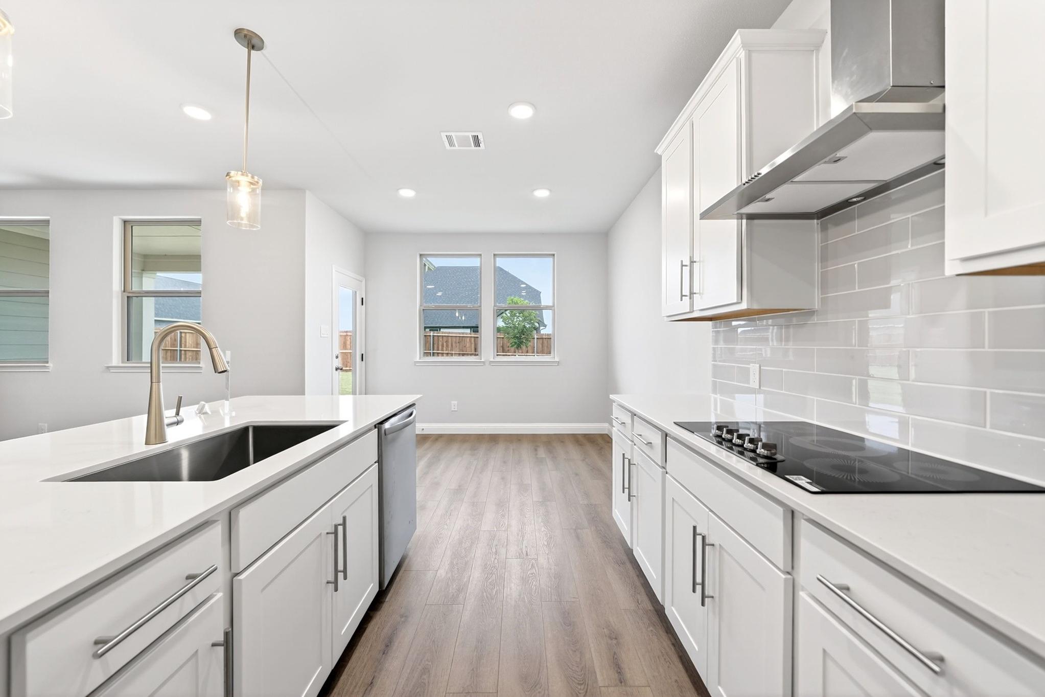 Modern kitchen in The Redbud floor plan featuring white cabinets, quartz countertops, and an open-concept dining area.