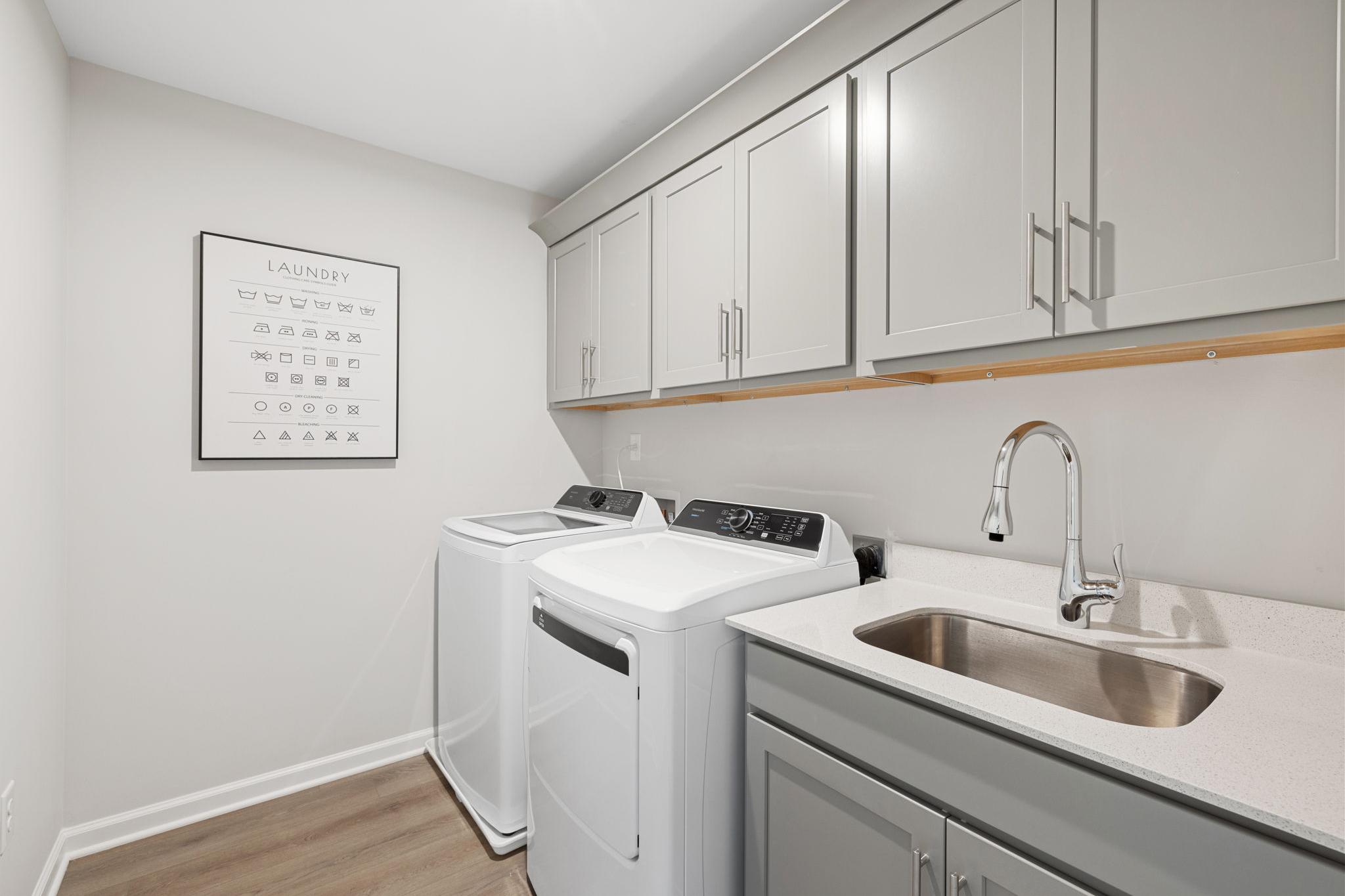 Laundry room at Lake Shore in Winder GA by Davidson Homes with white washer dryer, gray cabinets, utility sink, hardwood floors