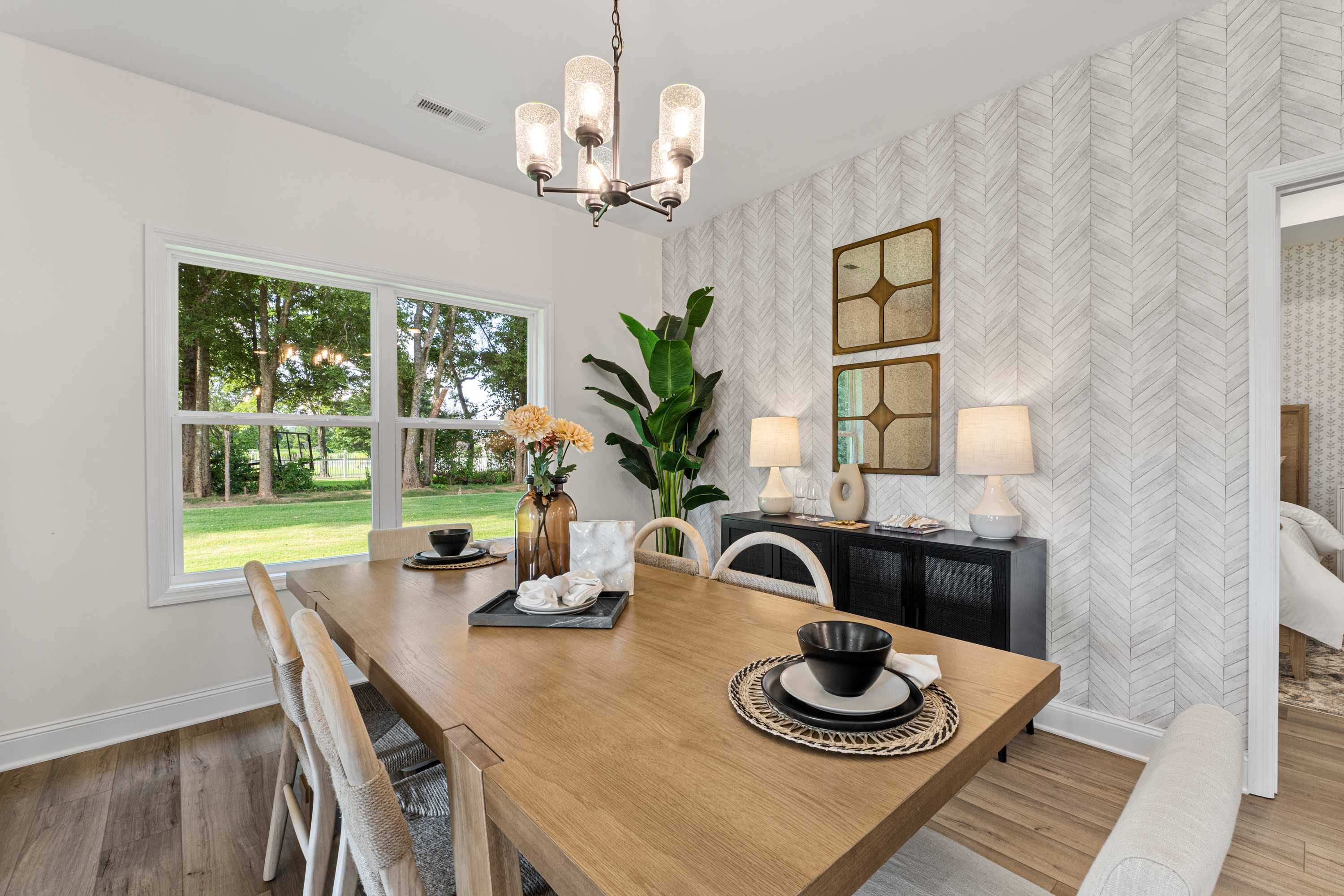 Spacious dining room at Lynn Meadows in Meridianville AL with wooden table, chevron wallpaper, potted plant, and garden views through large windows