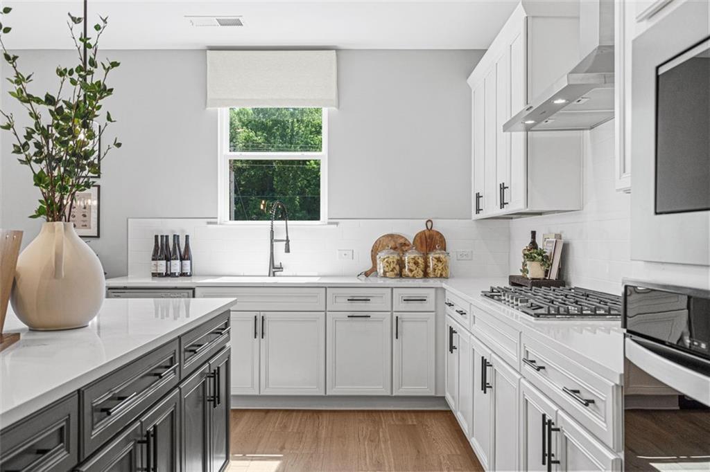 Modern white kitchen with shaker cabinets, dark island, stainless appliances, and window view in The Hickory B home, Hoschton, GA