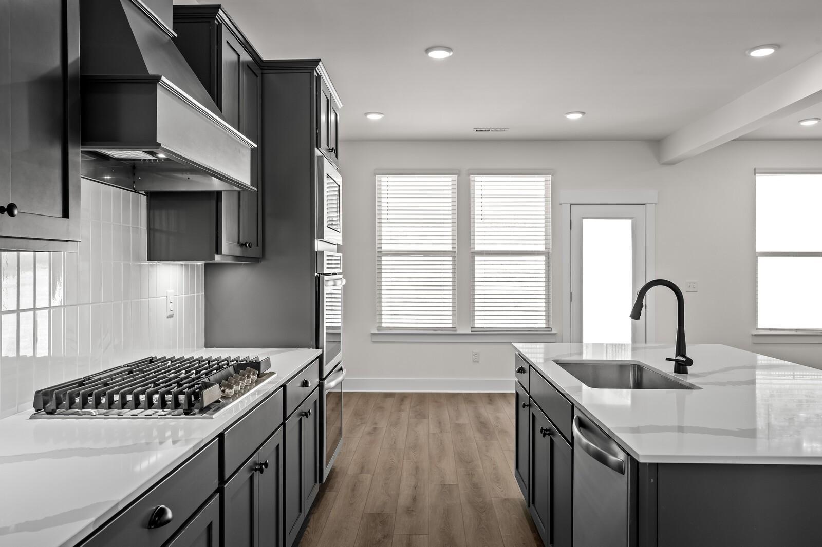 Modern kitchen with dark cabinets, quartz island, and gas range in The Willow floor plan at Woods Crossing, Gallatin, TN.