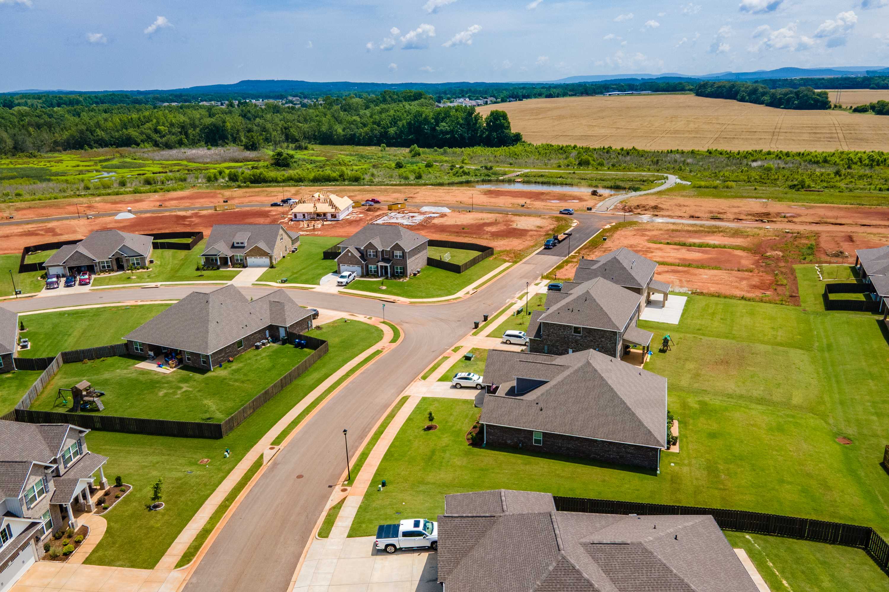 Aerial view of Barnett's Crossing in Madison Alabama with new homes under construction, green lawns, and surrounding fields