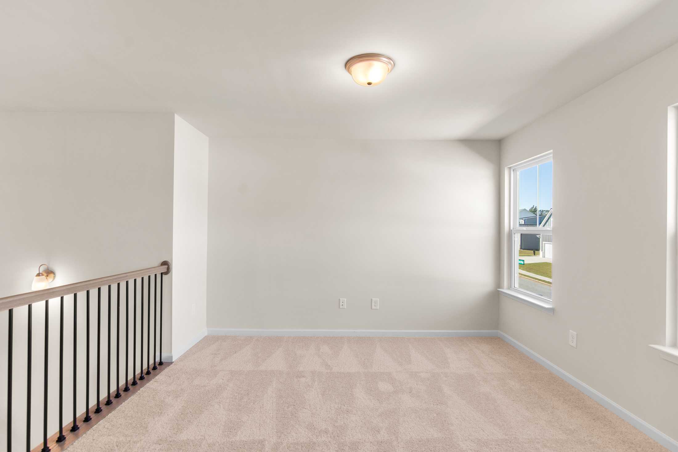 Spacious upstairs loft in The Willow B at Wehunt Meadows with beige carpet, black metal railing, and large window overlooking Hoschton, GA home
