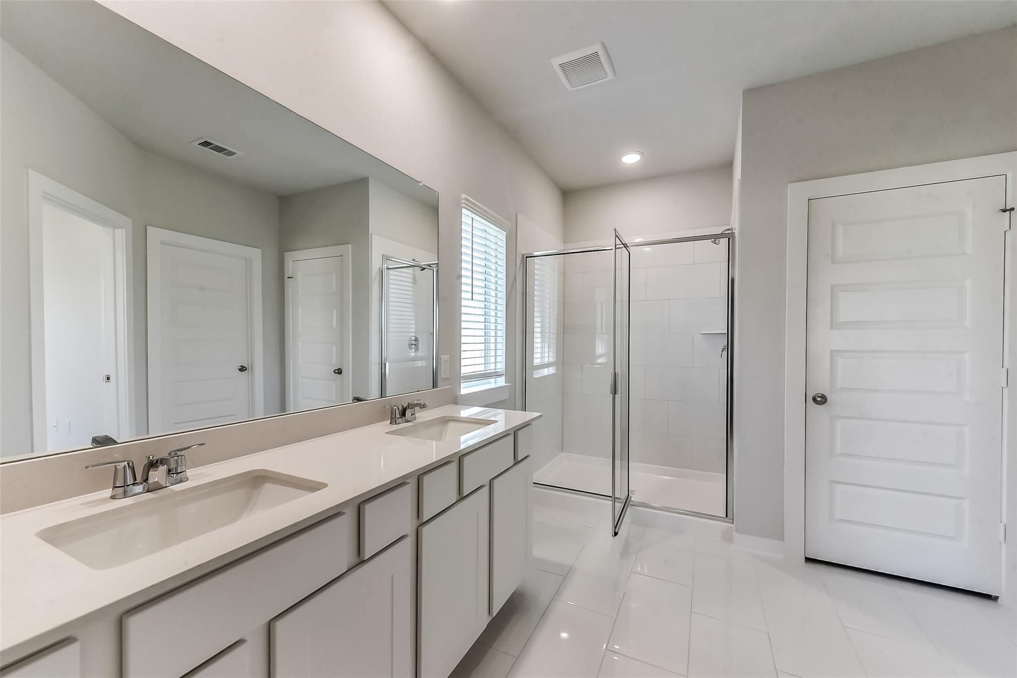 Modern master bathroom featuring double vanity with quartz countertop, large mirror, and frameless glass shower in Davidson Homes The Costa C, Dayton, Texas