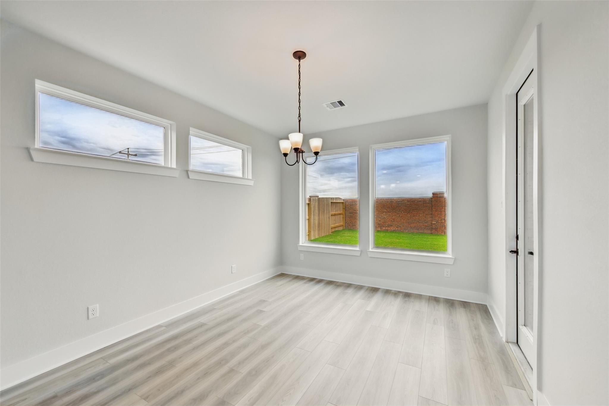 Bright sunroom with large windows, chandelier, and wood floors overlooking green backyard in Davidson Homes The Victoria C, Lago Mar