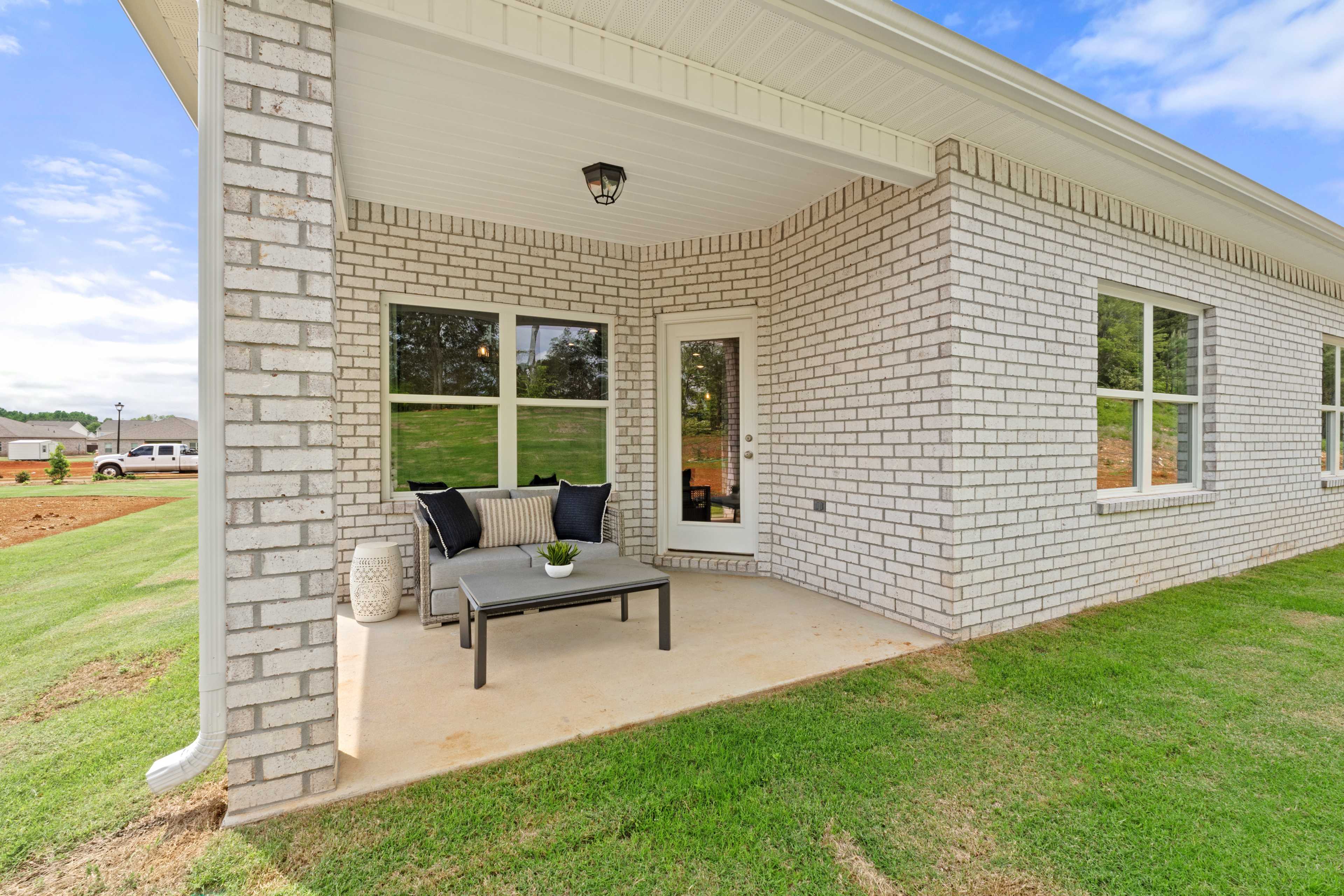 Covered patio with gray sofa and glass table at Ivy Hills in Toney, Alabama, brick home exterior and green lawn