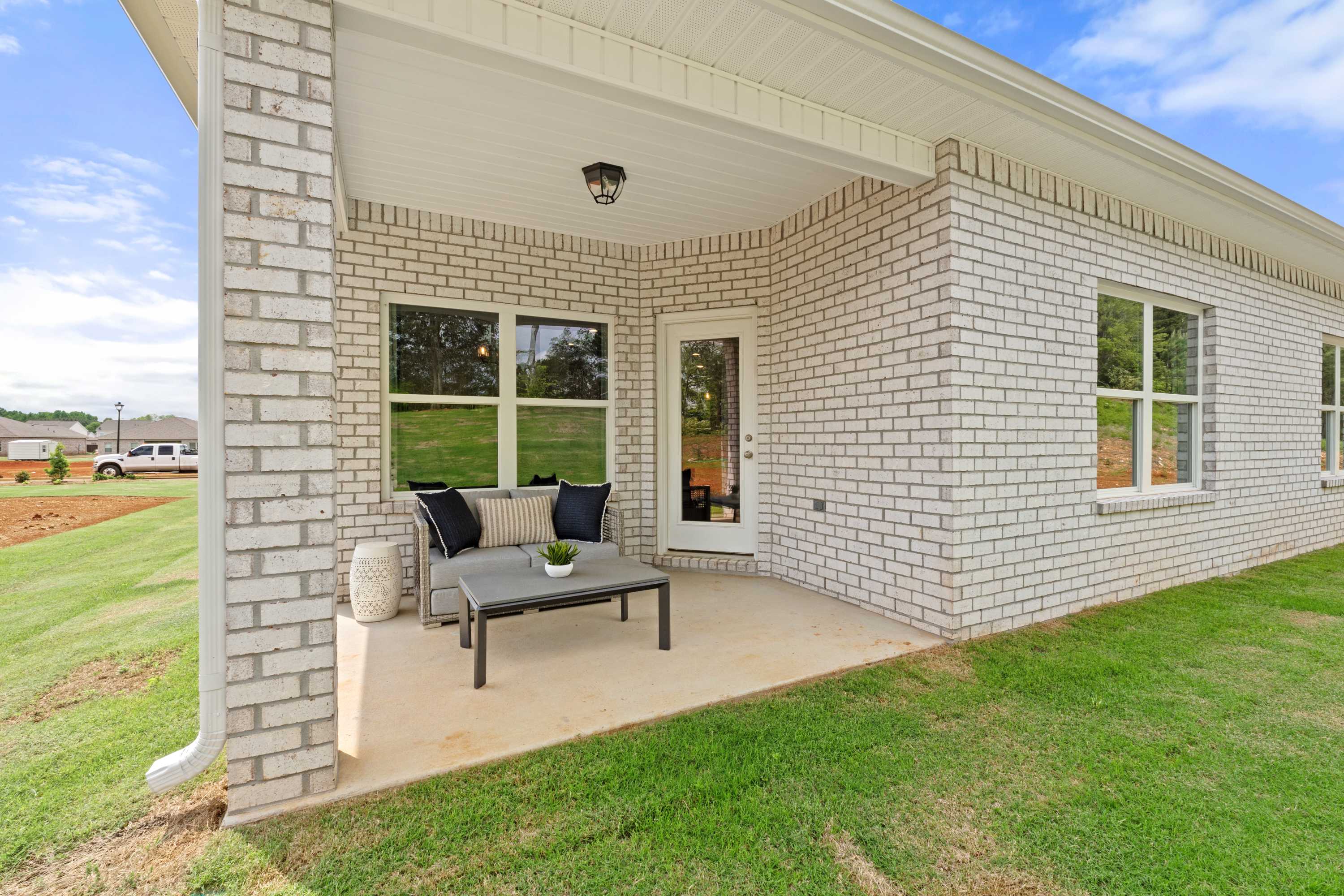 Covered patio with gray sofa and glass table at Ivy Hills in Toney, Alabama, brick home exterior and green lawn