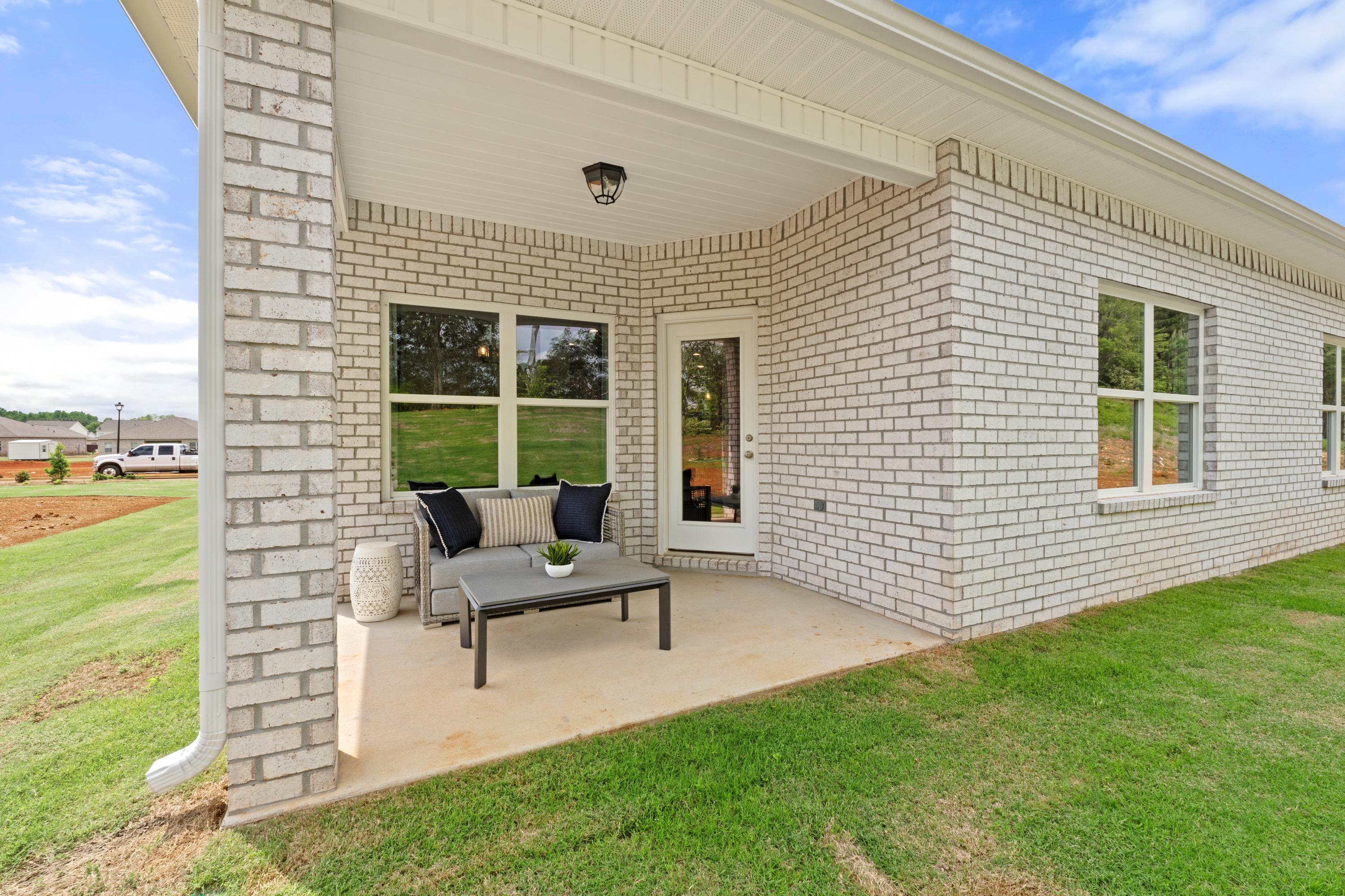 Covered patio with gray sofa and glass table at Ivy Hills in Toney, Alabama, brick home exterior and green lawn
