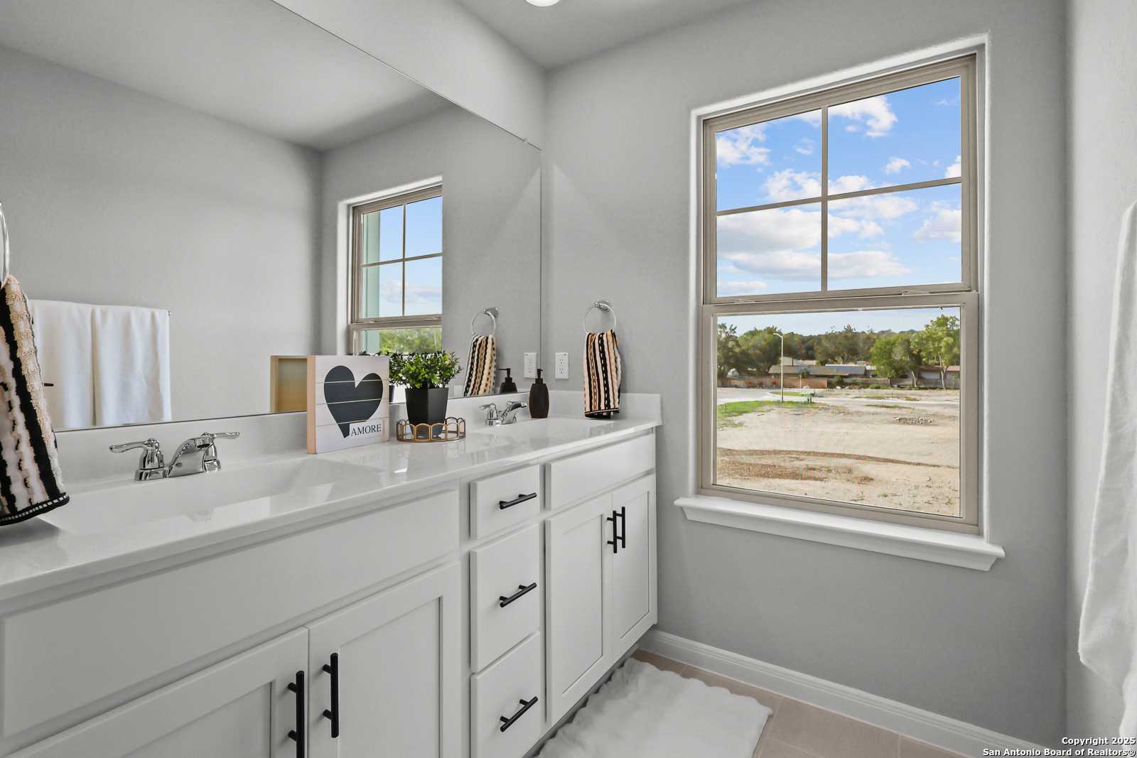 Modern double vanity bathroom with white cabinets, large window view, and plants in Davidson Homes Gillian C, San Antonio